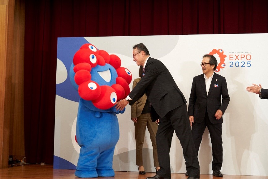 ミャクミャクと握手を交わす岡田大臣